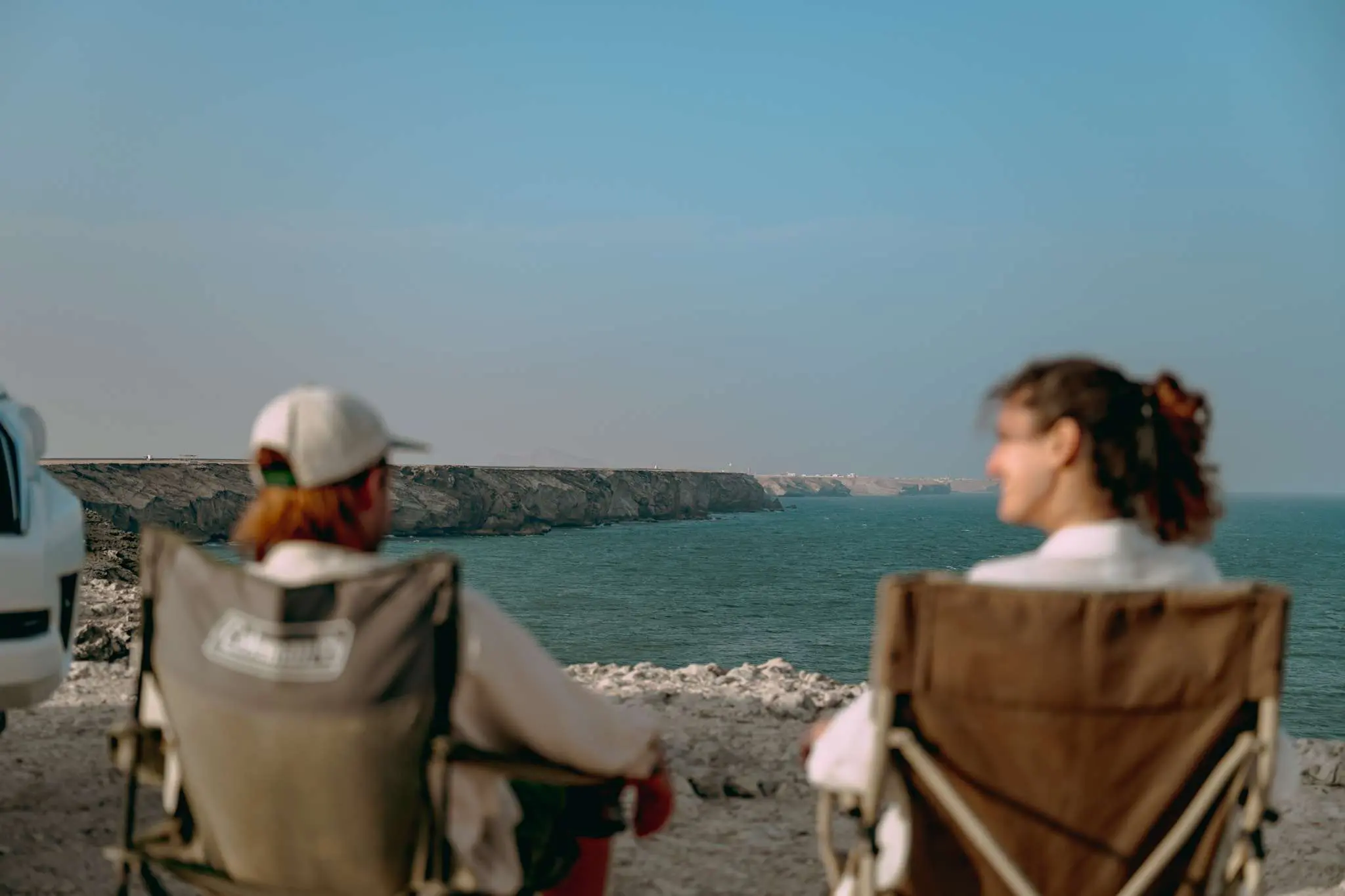 Twee mensen zitten in campingstoelen met uitzicht op de zee.