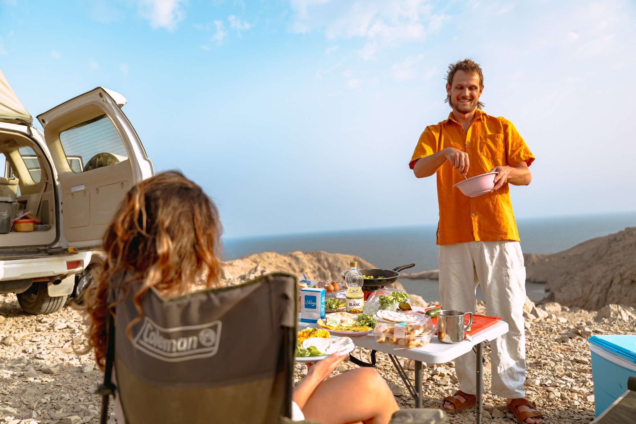 Two people sitting in camping chairs facing the sea.